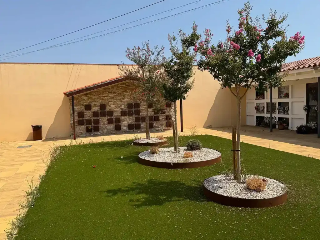 Jardín del cementerio de Vilamalla con alcorques de acero corten y, al fondo, el muro de columbarios bajo la pérgola