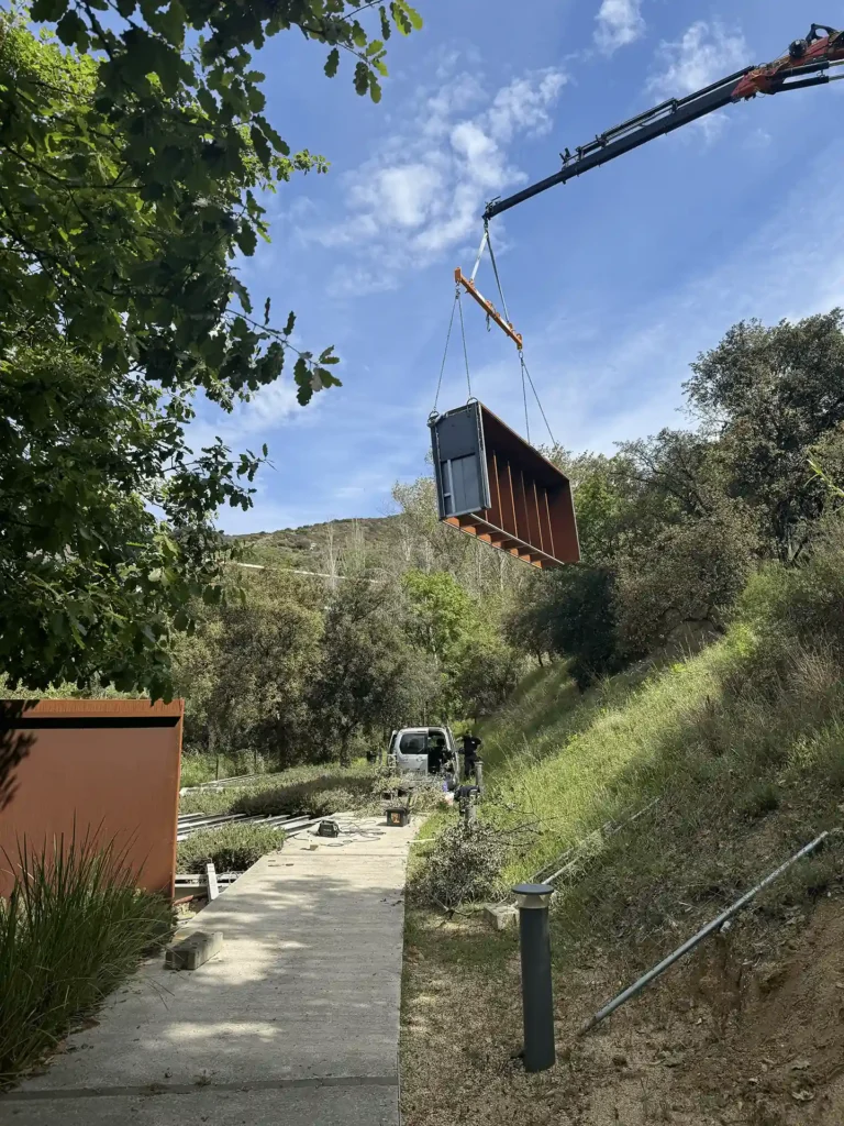 Grúa elevando un módulo completo de columbarios de acero corten en la obra del Tanatori de Badalona