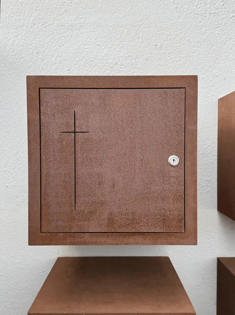 Detalle frontal de un columbario individual de acero corten, con la cruz calada y la cerradura